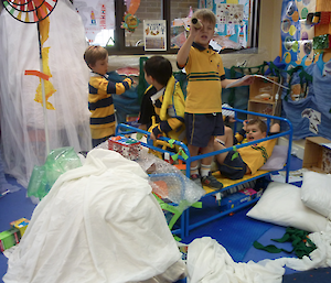 Little boys in a room full or toys, with one child in cot pretending it is a boat.