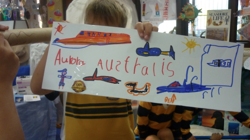 A child holding a cardboard picture of the ship and other little vehicles.