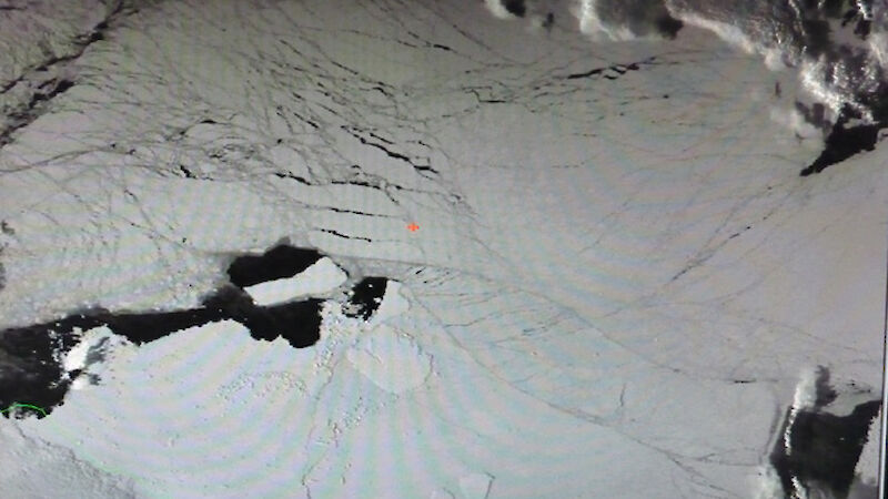 A high-up aerial view of the ice. The ship is a tiny red dot in the white.