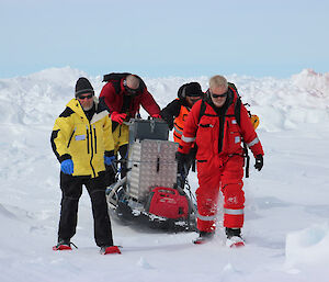 A group tows a big piece of machinery over the ice.