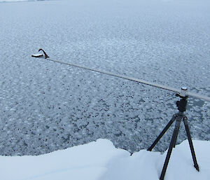 Tripod with long arm fixed to the top extends out over the icy water