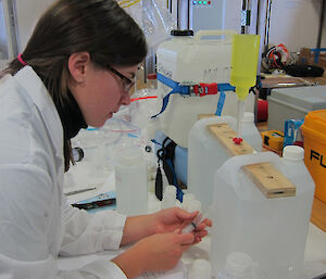 Scientist in lab coat holding a syringe with bottles of water close by on the bench.