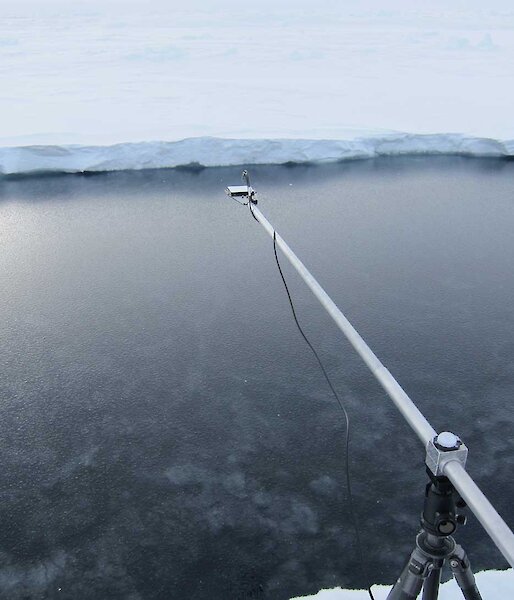 Arm on tripod extends out over clearer, less icy water.
