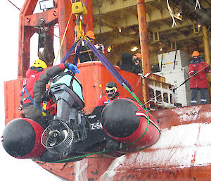 Red rubber boat being lowered over the side of the ship with a person inside it.