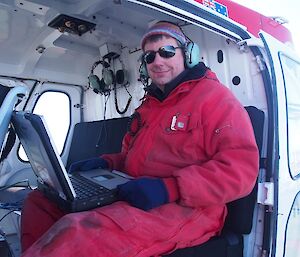 Scientist sitting in the heli with a computer on his lap.