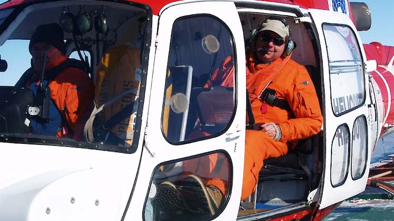 Helicopter on the deck of the ship with the door open and a man leaning out smiling