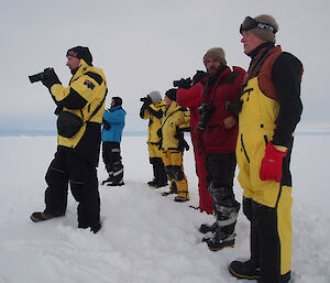 Expeditioners stand around the ice hole with their cameras ready to take a photo.