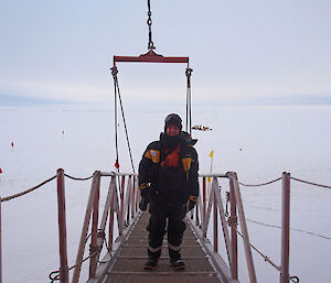 Wendy is dressed in layers of cold-weather gear standing on the gangway to the ship leading onto the ice with flags dotted on the ice behind.