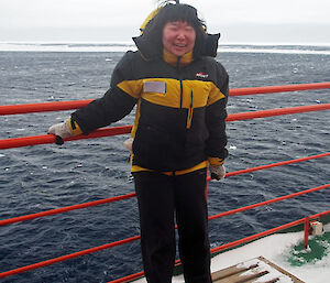 The female scientists is laughing while standing on the cold deck of the ship.