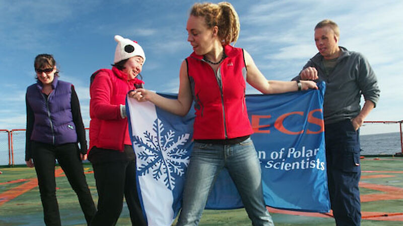 Early career scientists get tangled up in their new flag on the deck of the ship.