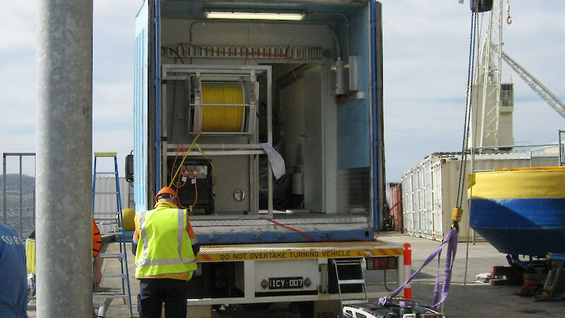 The Remotely Operated Vehicle attached to a crane in front of a shipping container.