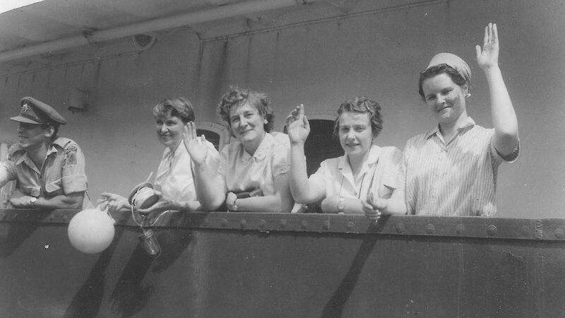 Four female researchers waving from deck of ship.
