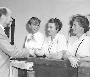 Man on wharf farewelling three women on deck of ship