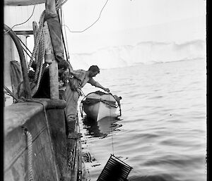A figure leans over the edge of a ship and dangles a rack of film plates tied to a rope into the ocean.