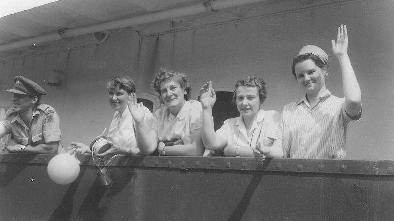 Four female researchers waving from deck of ship