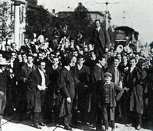 A black and white photo of Mawson being carried on a chair by a big crowd of his students.