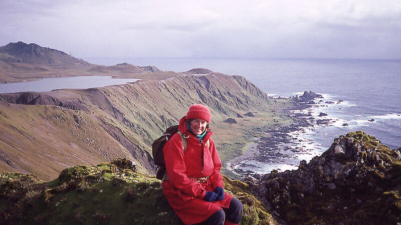 Scientist sitting at top of rocky cliff overlooking bay