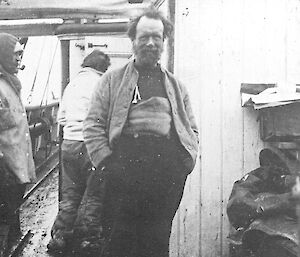 A black and white photograph of a man standing onboard a boat.