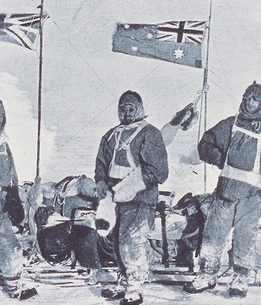Black and white photo of three men in old-fashioned polar clothes by a sledge.