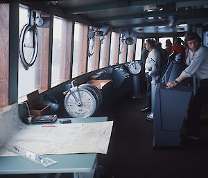 People stare out the widows of the bridge that has charts and instruments all round.