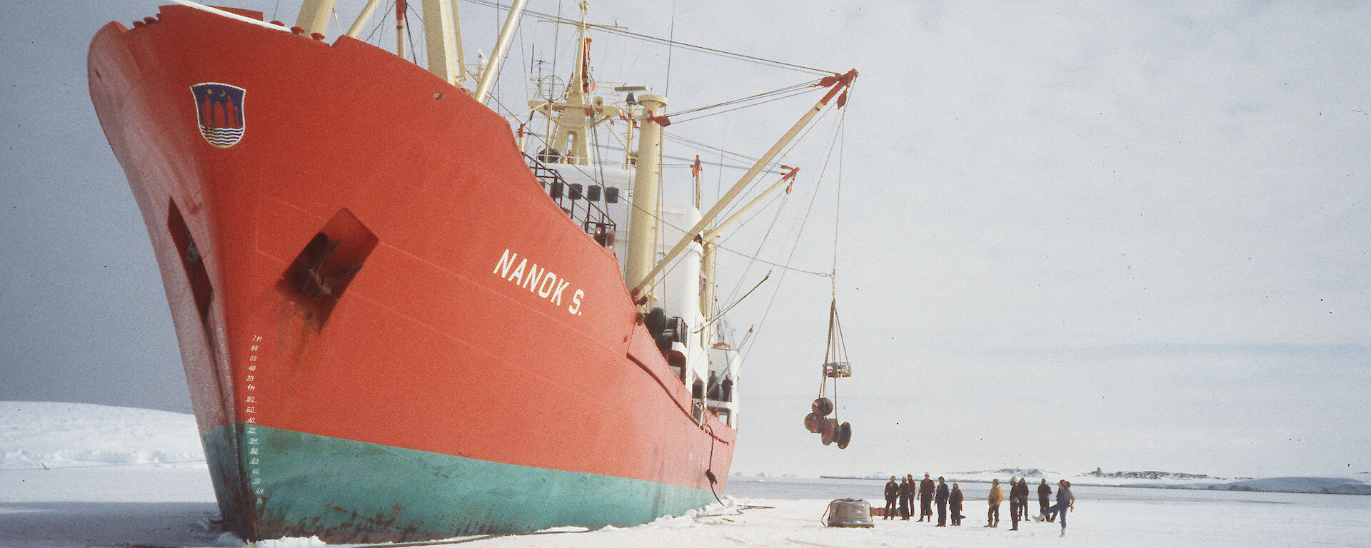 An orange ship unloading cargo with a crane onto the ice.