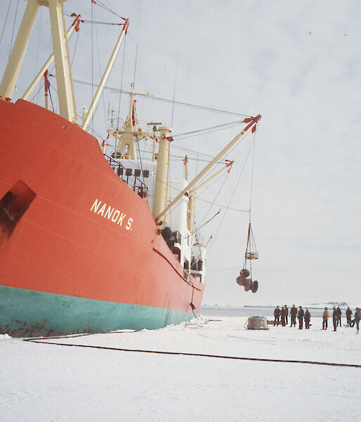 An orange ship unloading cargo with a crane onto the ice.