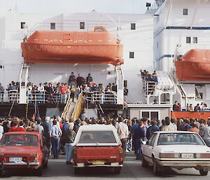Red ship by the dock with cars and onlookers.