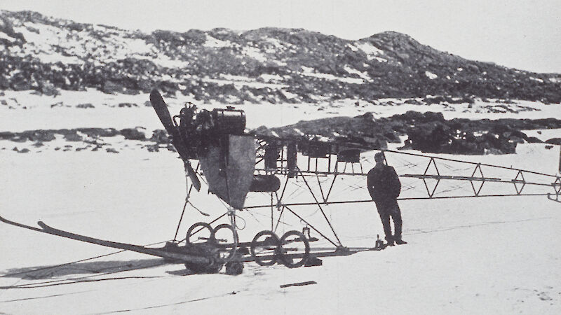 Man standing next to small long tractor adapted from monoplane engine and parts