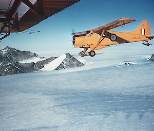 A yellow plane flying low over snow.