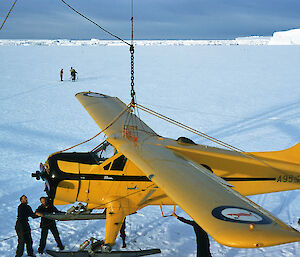 A small plane is moved by crane from a large ship onto ice and is guided by four men