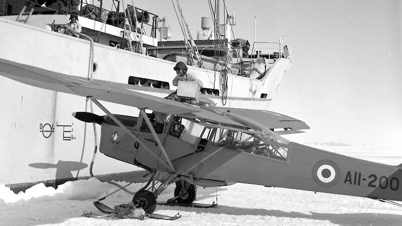 A vintage photo of a small, light plane on ice next to a large ship