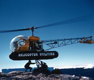 Expeditioner removing sling load from Bell 47G-2 helicopter