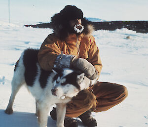Man in snow with husky, his beard icy, leans on the dog