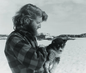 An expeditioner in profile holds a husky pup