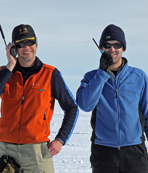 Two expeditioners talk into hand-held radios.