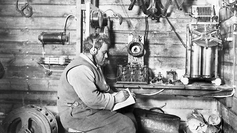Profile of a young man wearing headphones taking notes while seated next to a radio in a mechanics workshop.