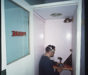 A man stands up to talk on a phone in a small, bare room.