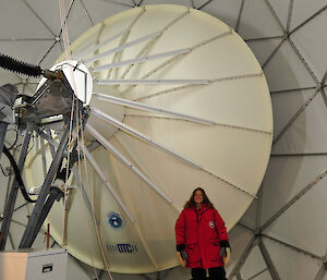 Expeditioner wearing a red coat standing in front of a large satellite dish.