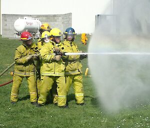 Five people in fire fighting gear cluster together holding a powerful water hose
