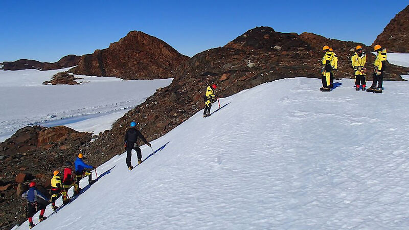 View of six expeditioners climbing steep ice slope with ice free hill behind