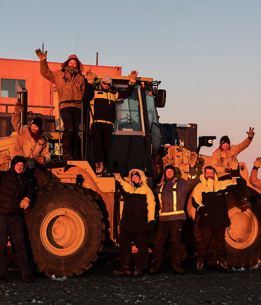 Group of expeditioners standing near loader waving at the camera at sunset