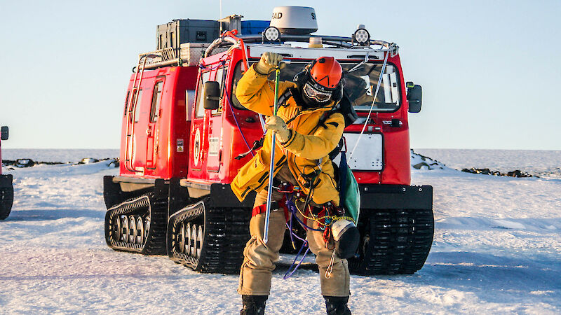Expeditioner with safety ropes attached to oversnow vehicle using long probe to test the ice