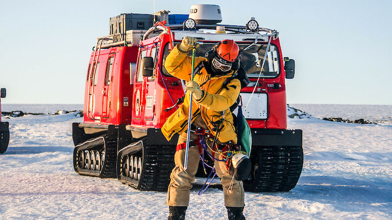 Expeditioner with safety ropes attached to oversnow vehicle using long probe to test the ice