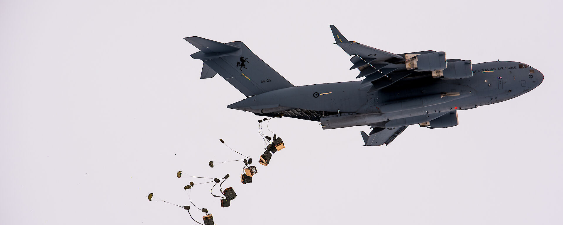 Pallets of supplies attached to parachutes drop from the tail end of a C-17A aircraft.