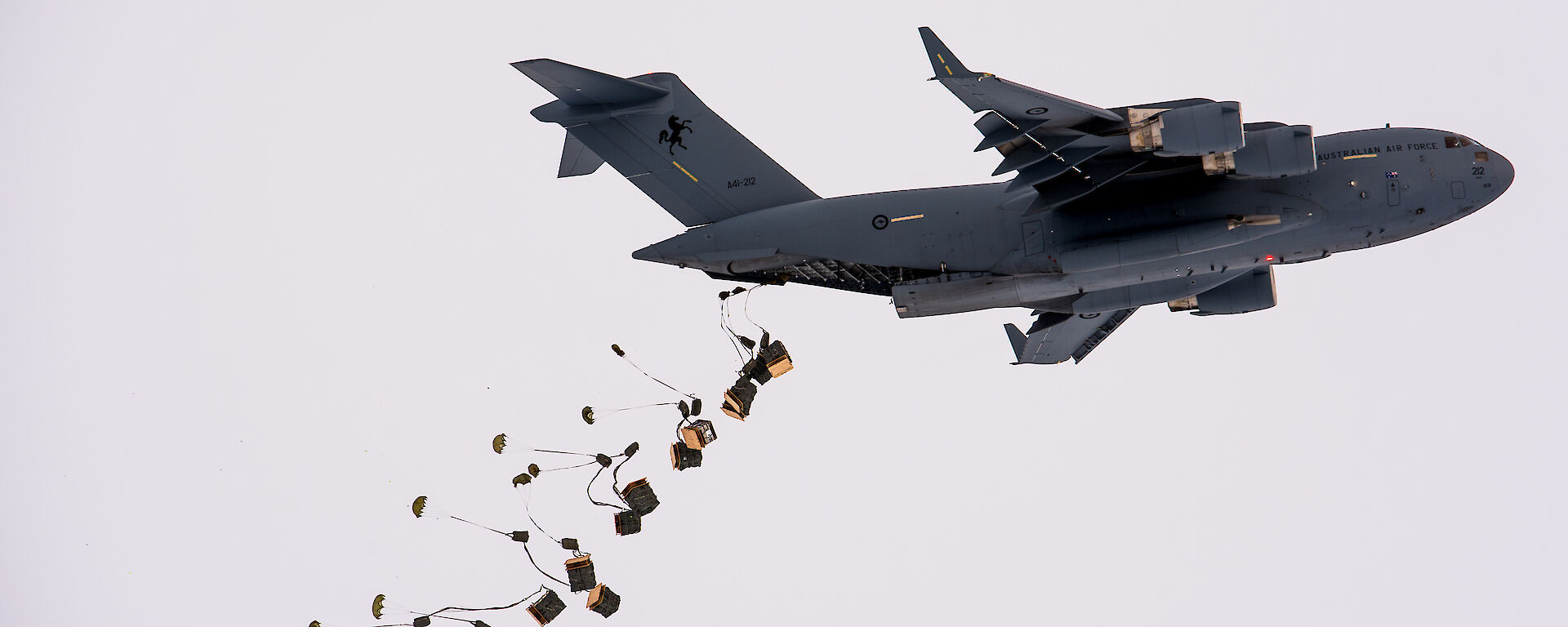 Pallets of supplies attached to parachutes drop from the tail end of a C-17A aircraft
