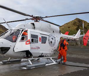A close-up of a white helicopter being refuelled by a man in an orange suit.