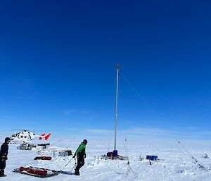 A helicopter on endless snow with scientists dragging a sled in the foreground