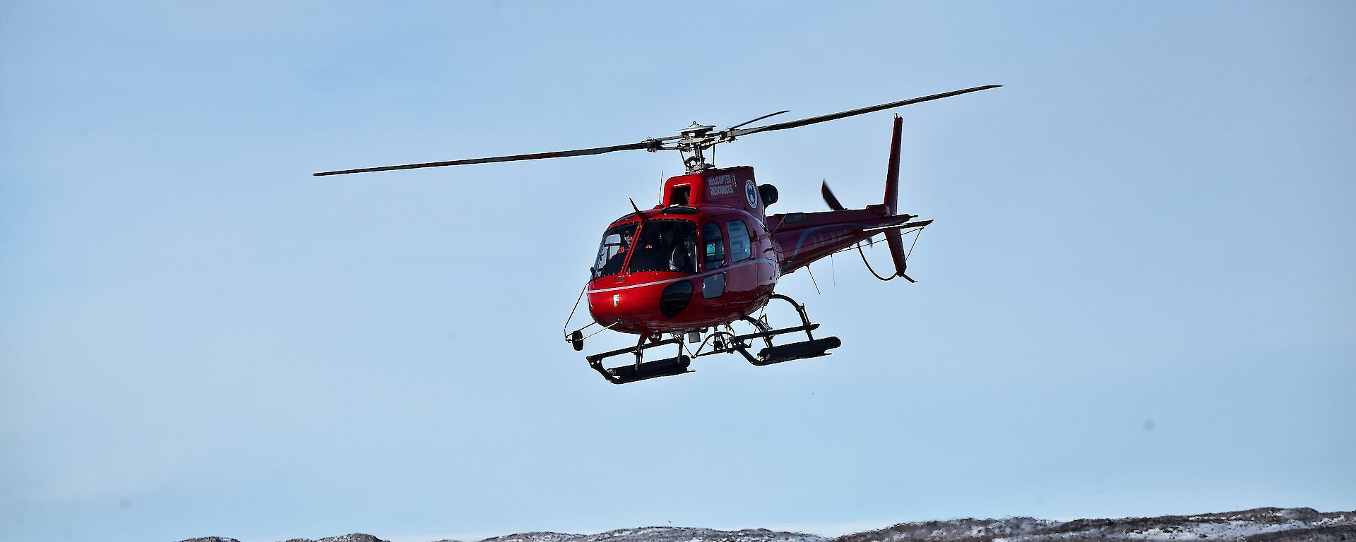 AS350B3 helicopter hovers over the snow dusted ground.