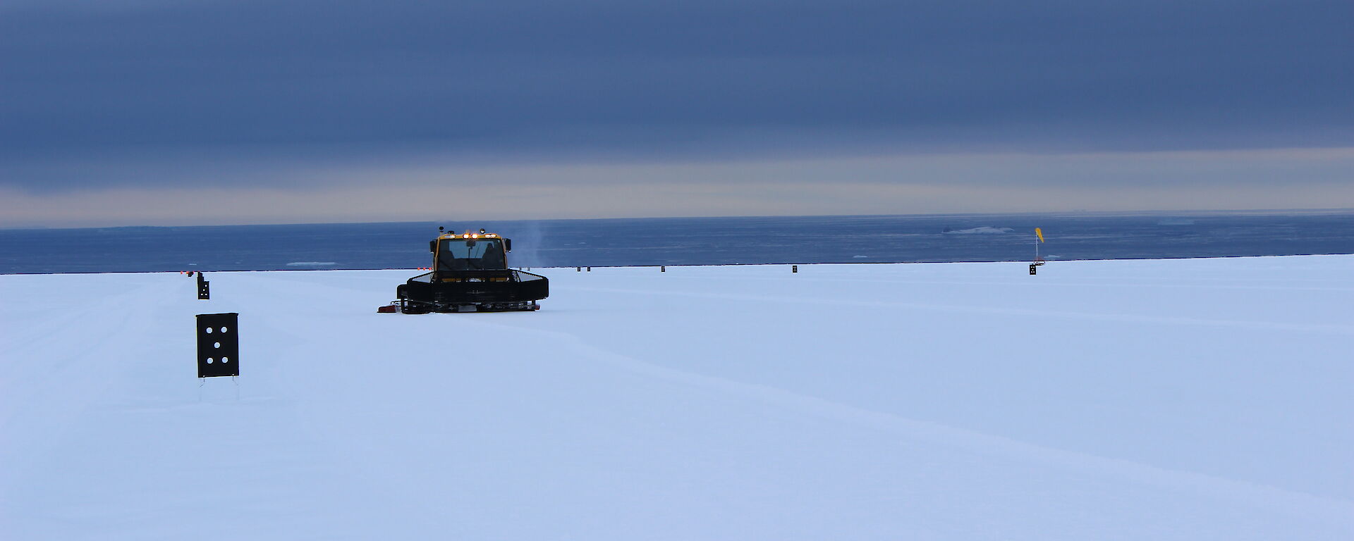 A flat expanse of Antarctic plateau with sea in background, featuring a spaceship like tracked vehicle attending the runway