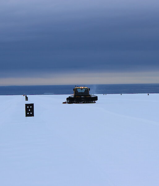 A flat expanse of Antarctic plateau with sea in background, featuring a spaceship like tracked vehicle attending the runway